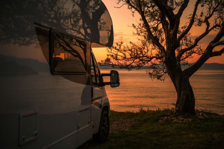 Autocaravana en un lago con la puesta de sol al fondo.